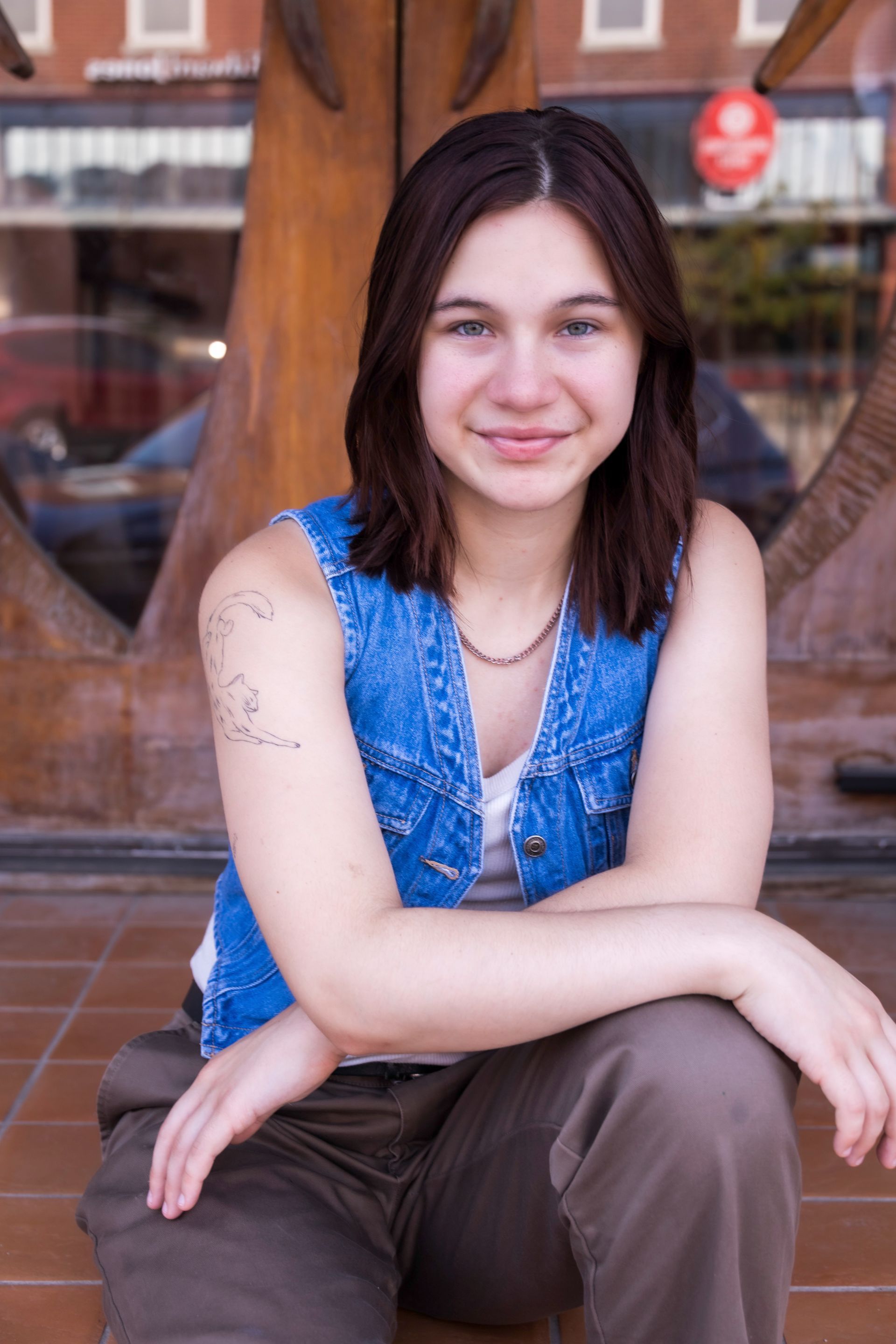 A woman wearing a denim vest is sitting on the ground with her arms crossed