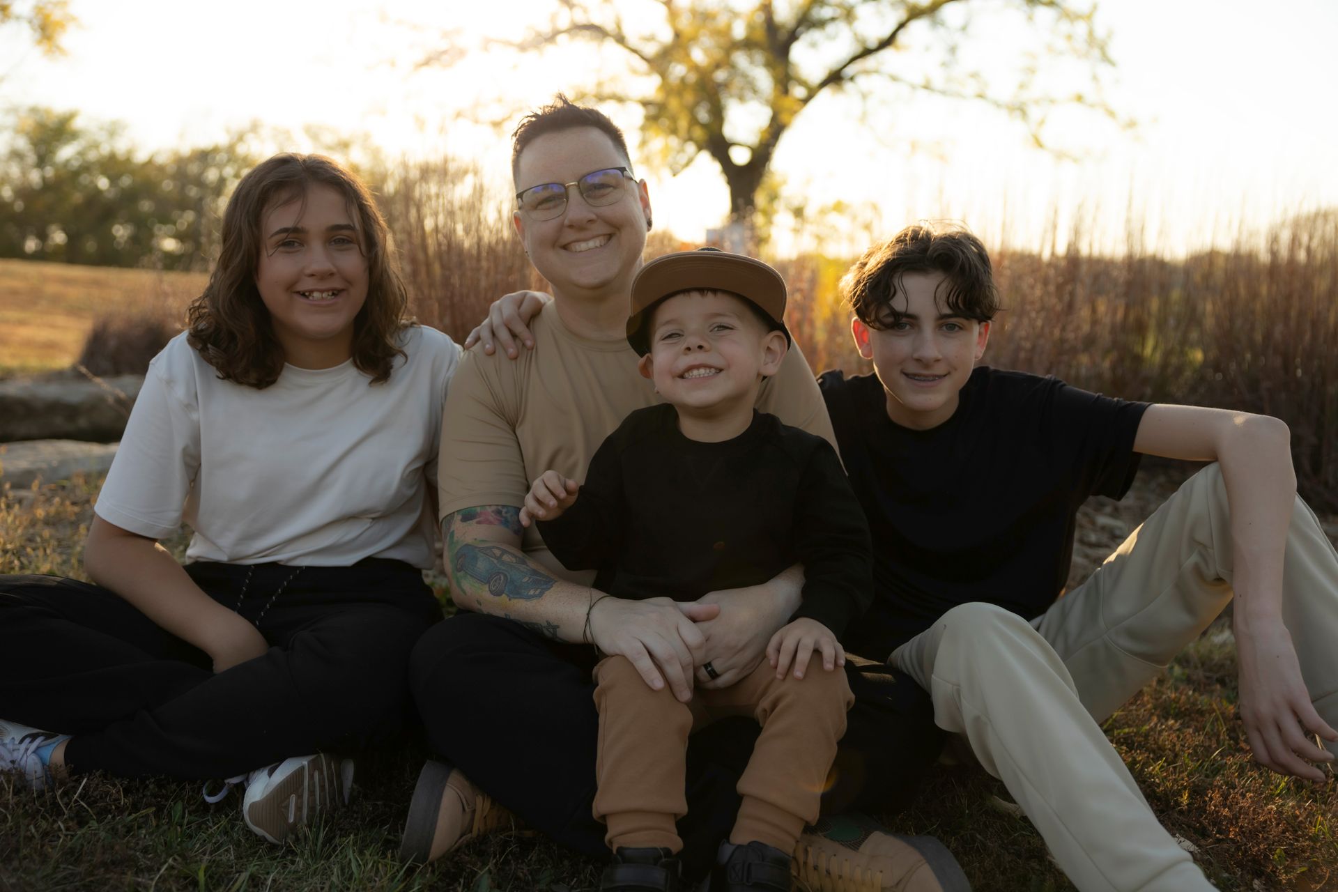 A man and three children are posing for a picture while sitting in the grass.