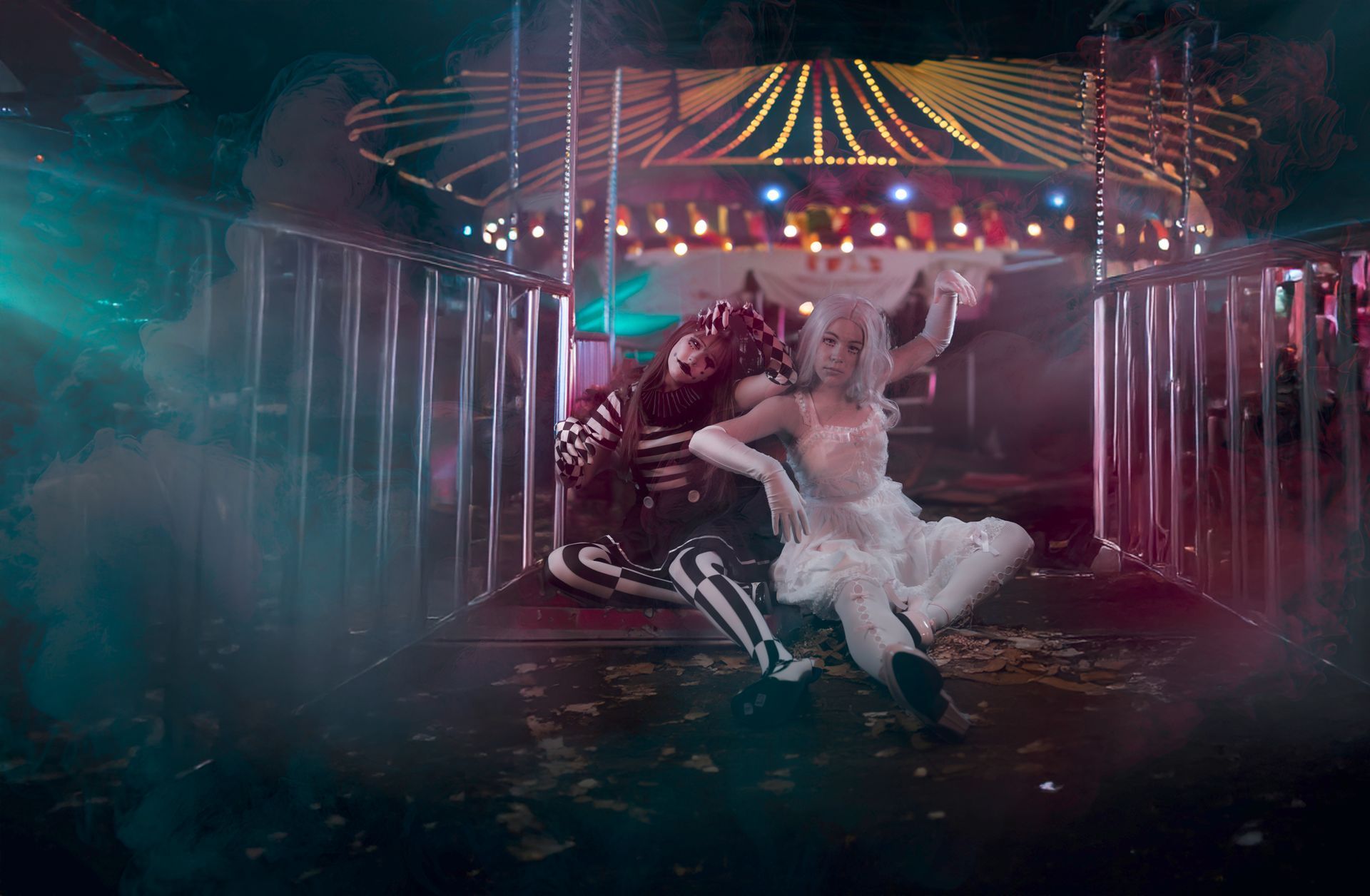 Two costumed figures dance in front of a carousel. One wears a skeleton suit, the other a white tutu.