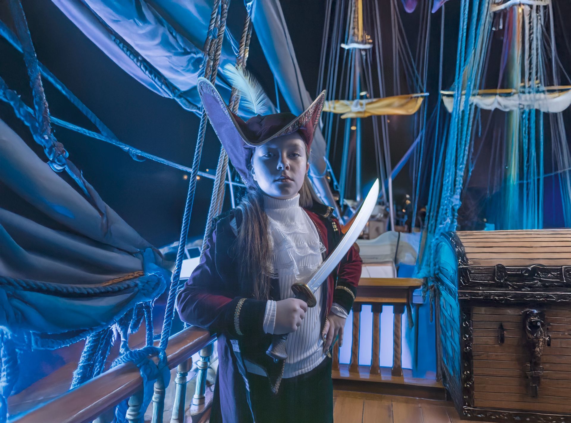 Person in pirate attire holds a sword on a ship deck, blue lighting.