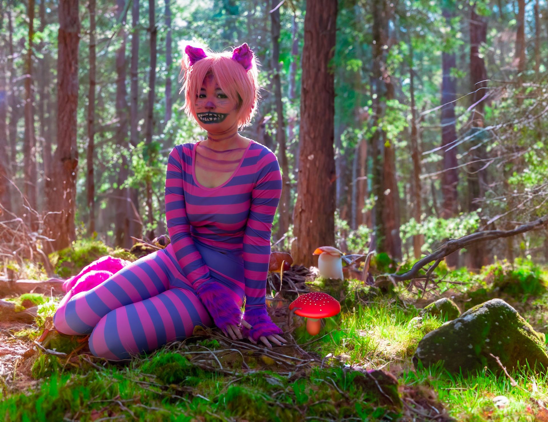 A woman in a cheshire cat costume is sitting in the woods.