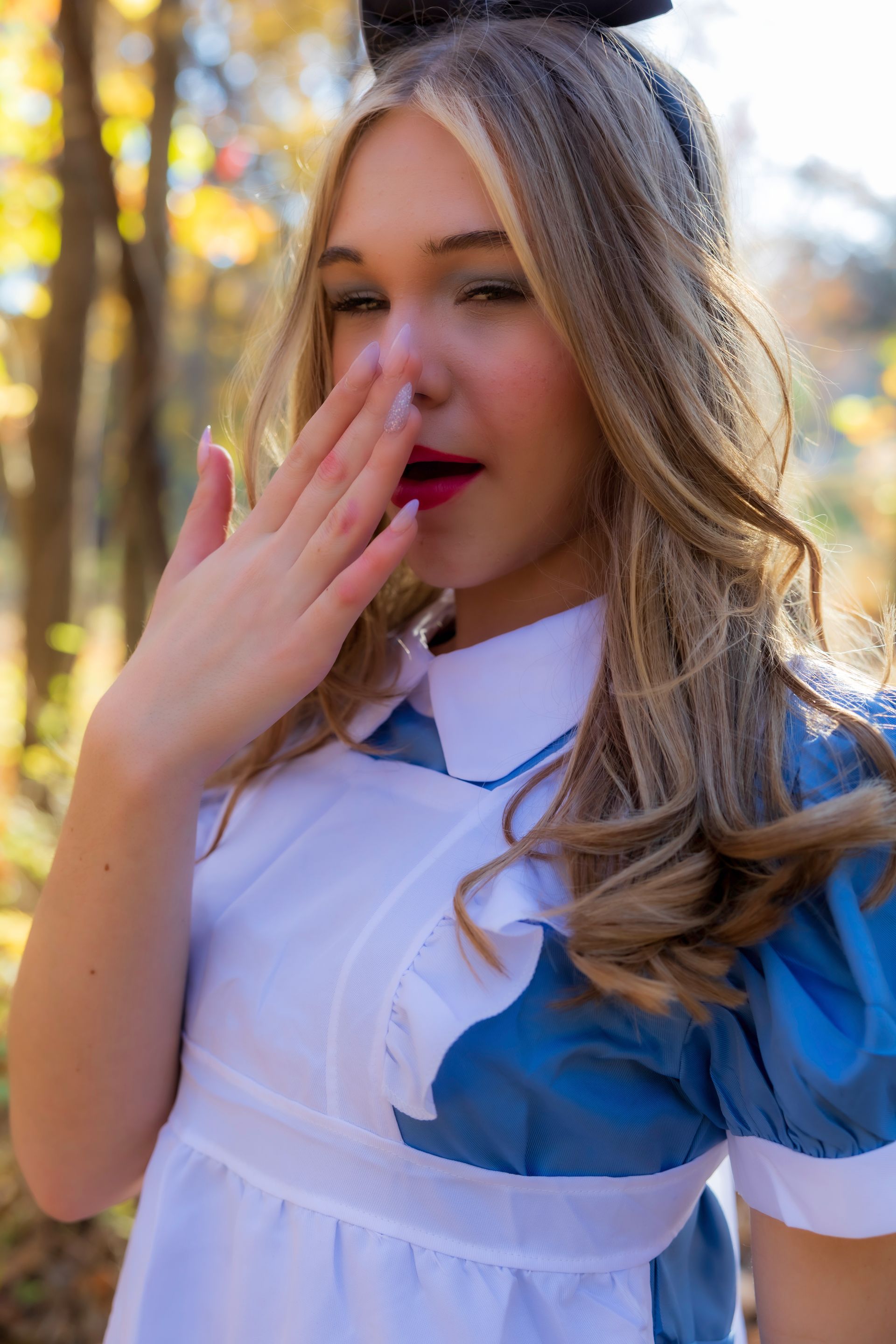 A woman in a alice in wonderland costume is covering her mouth with her hand.