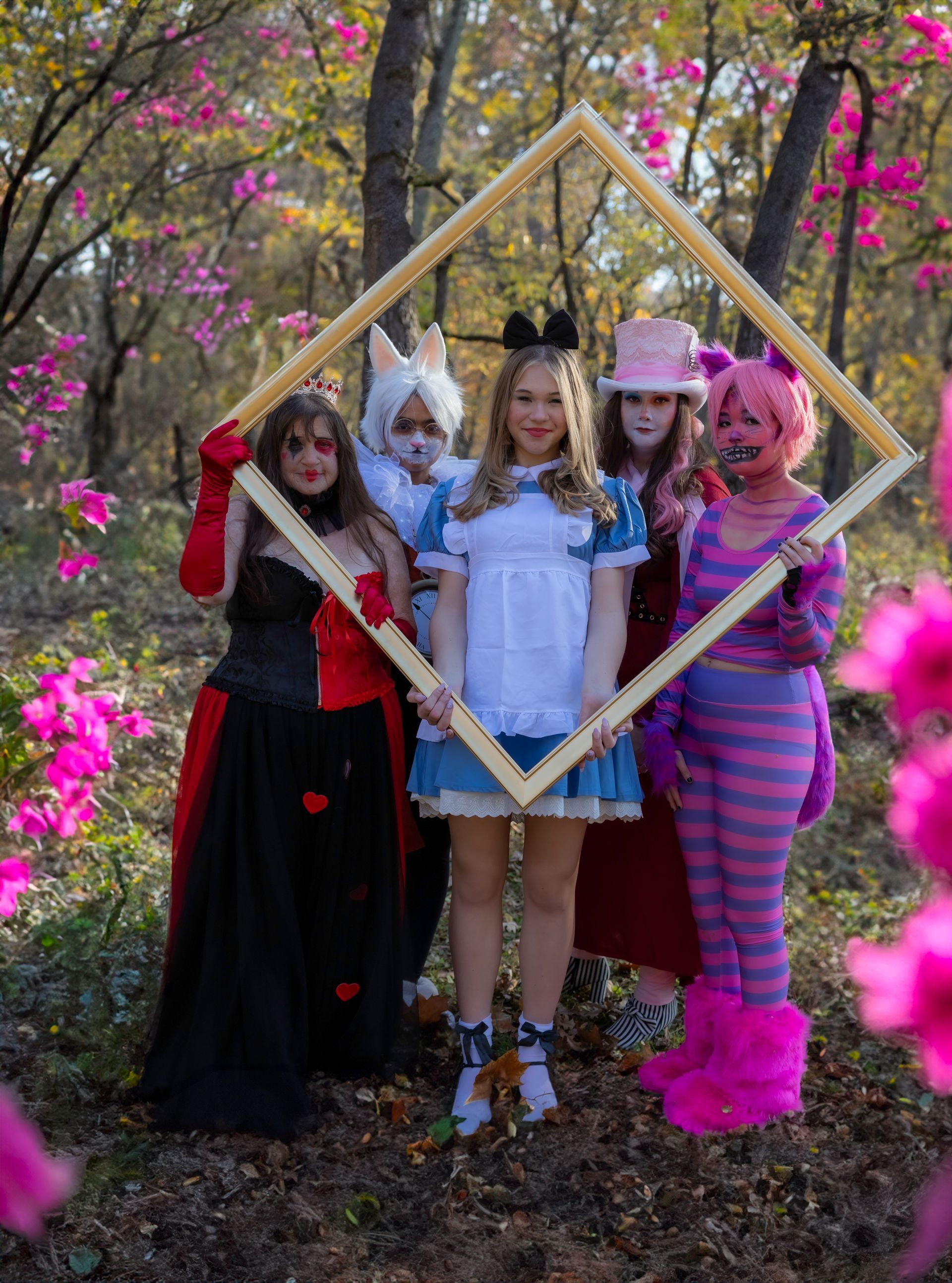 A group of women dressed in alice in wonderland costumes are posing for a picture in the woods.