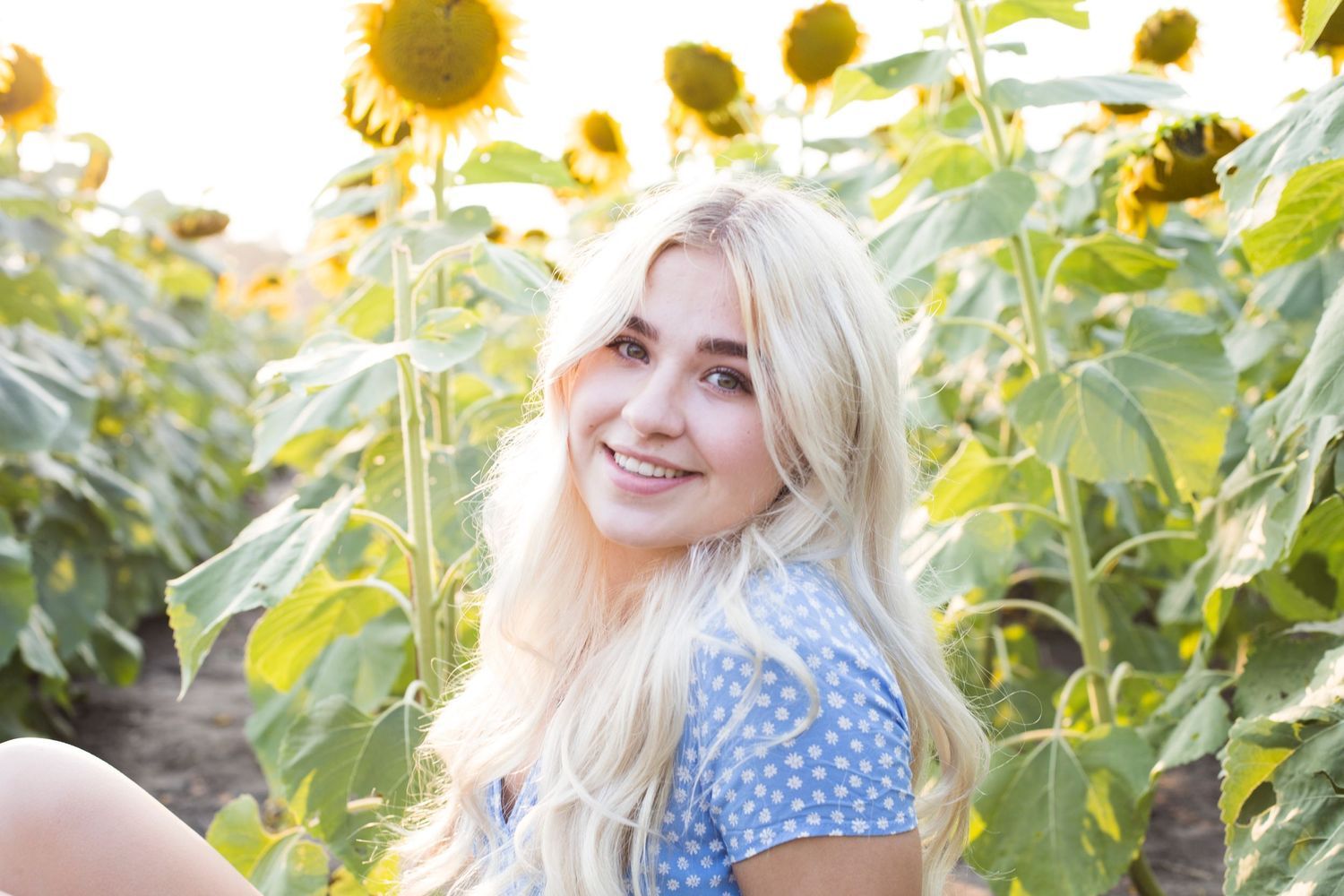 A woman is sitting in a field of sunflowers and smiling.