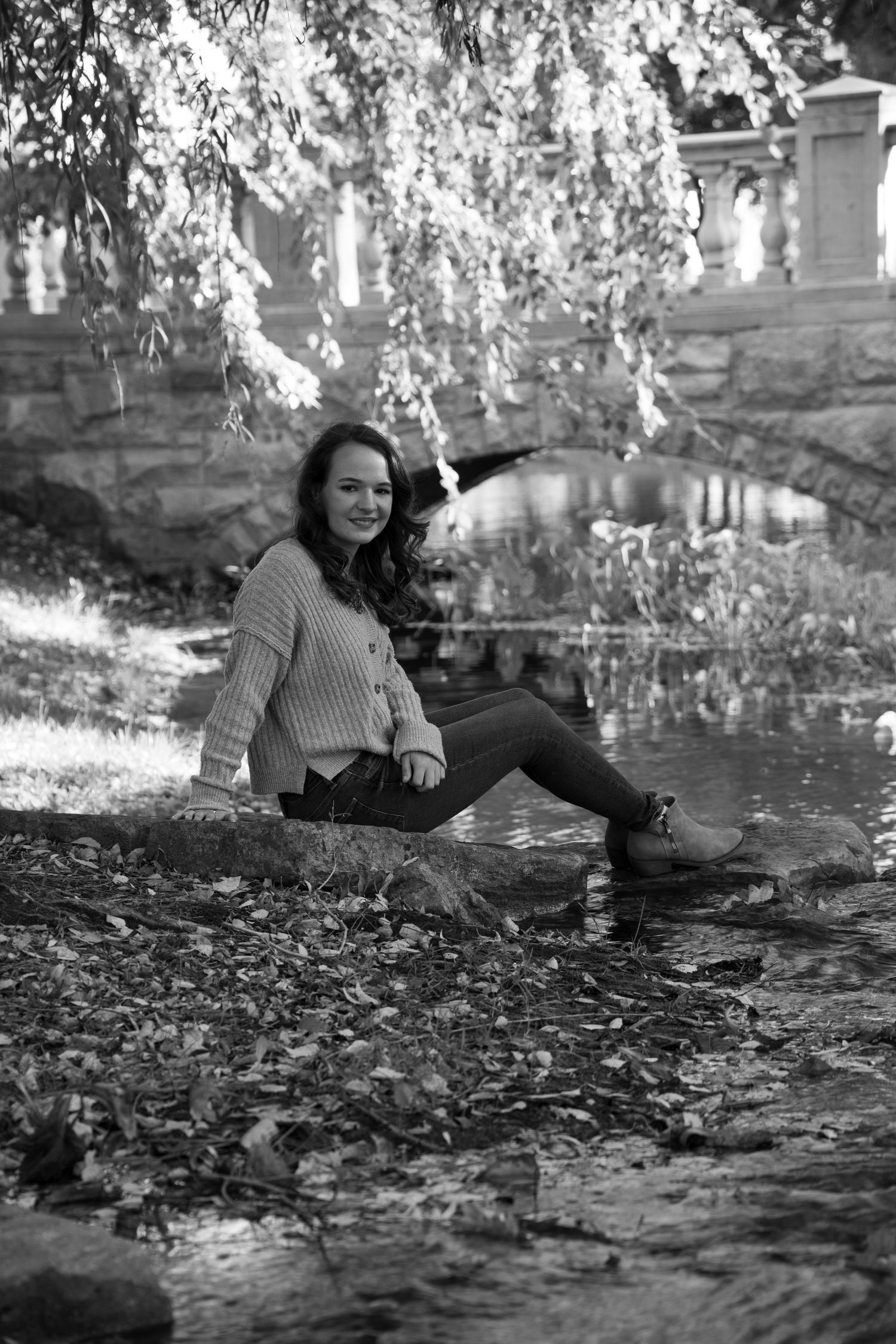 A woman is sitting on a rock near a river in a black and white photo.