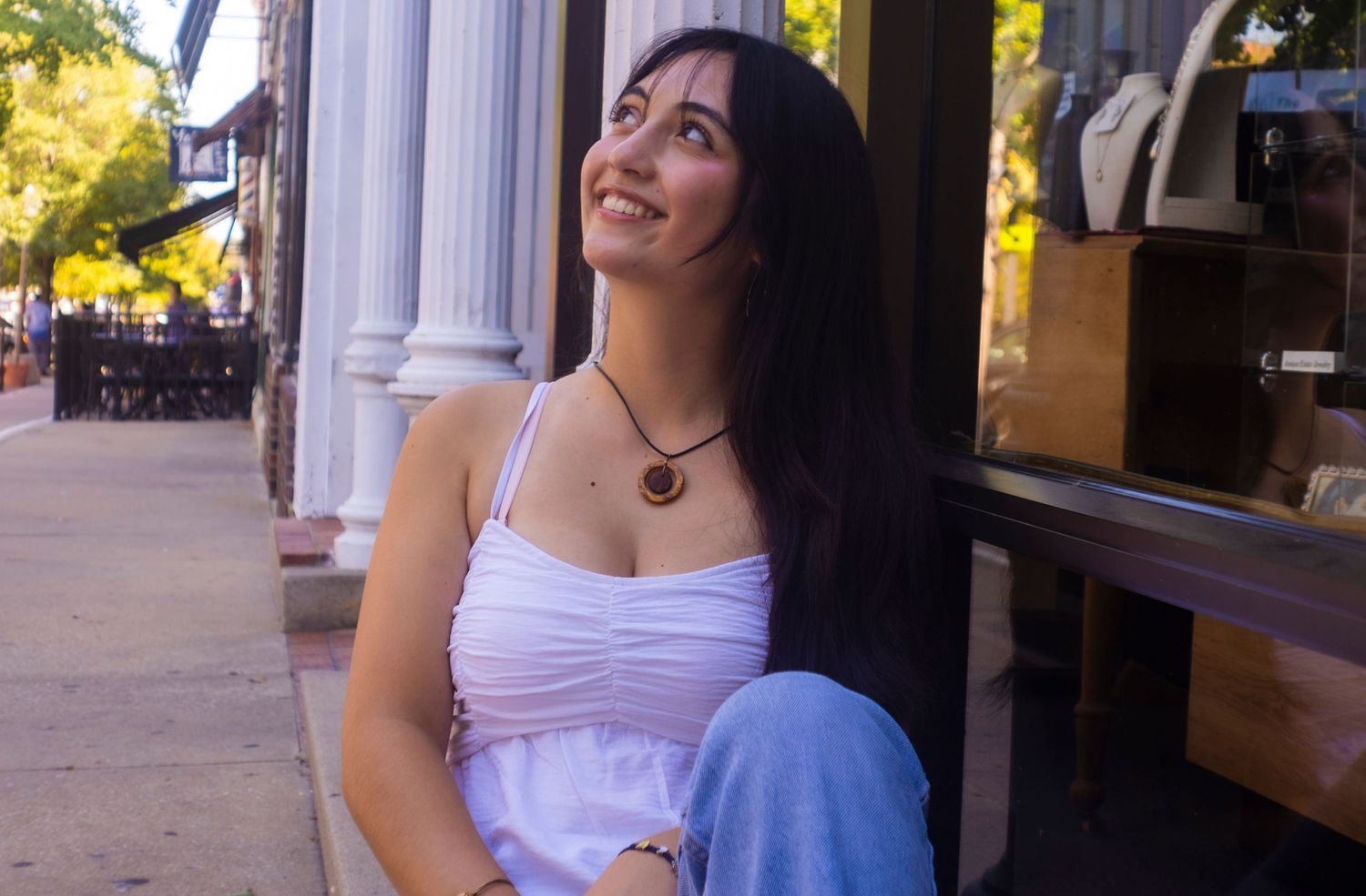 A woman in a white dress is sitting on the sidewalk looking up.