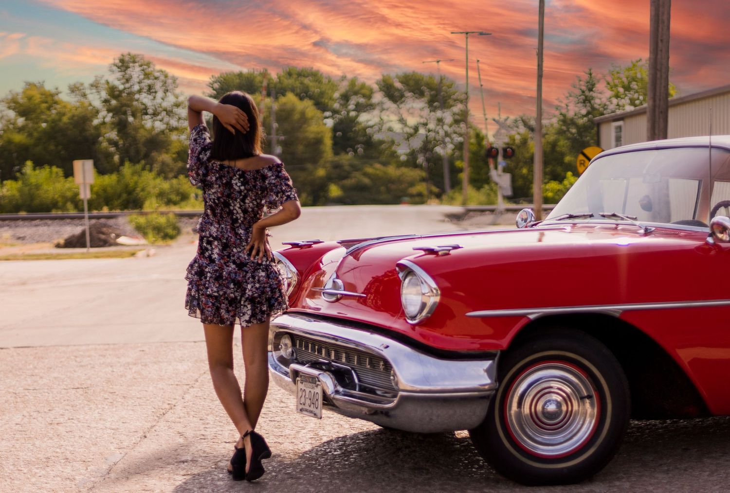 A woman in a dress is standing next to a red car.