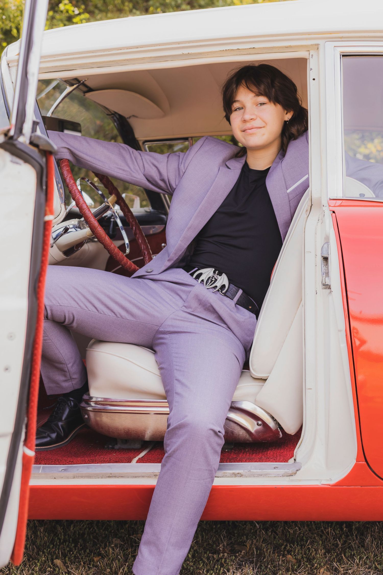 A woman in a purple suit is sitting in the driver 's seat of a red car.