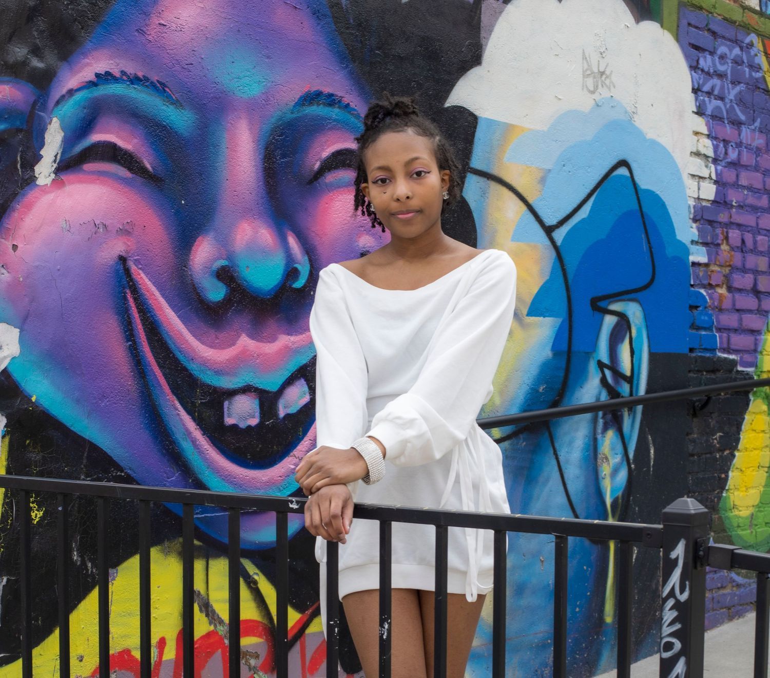 A woman in a white dress is standing in front of a graffiti wall.