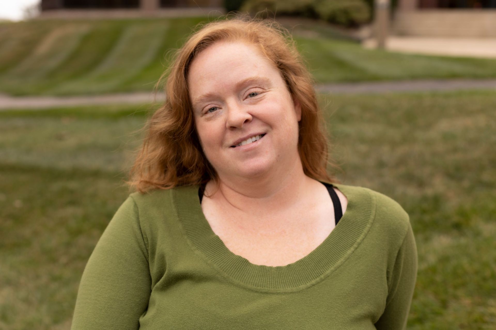 The woman is wearing a green sweater and smiling for the camera.