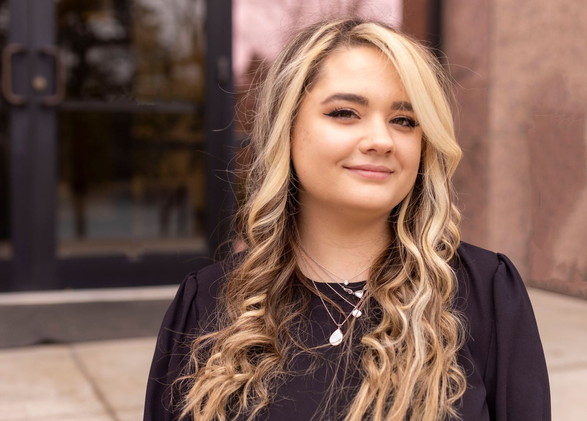 A woman with long blonde hair is standing in front of a building.