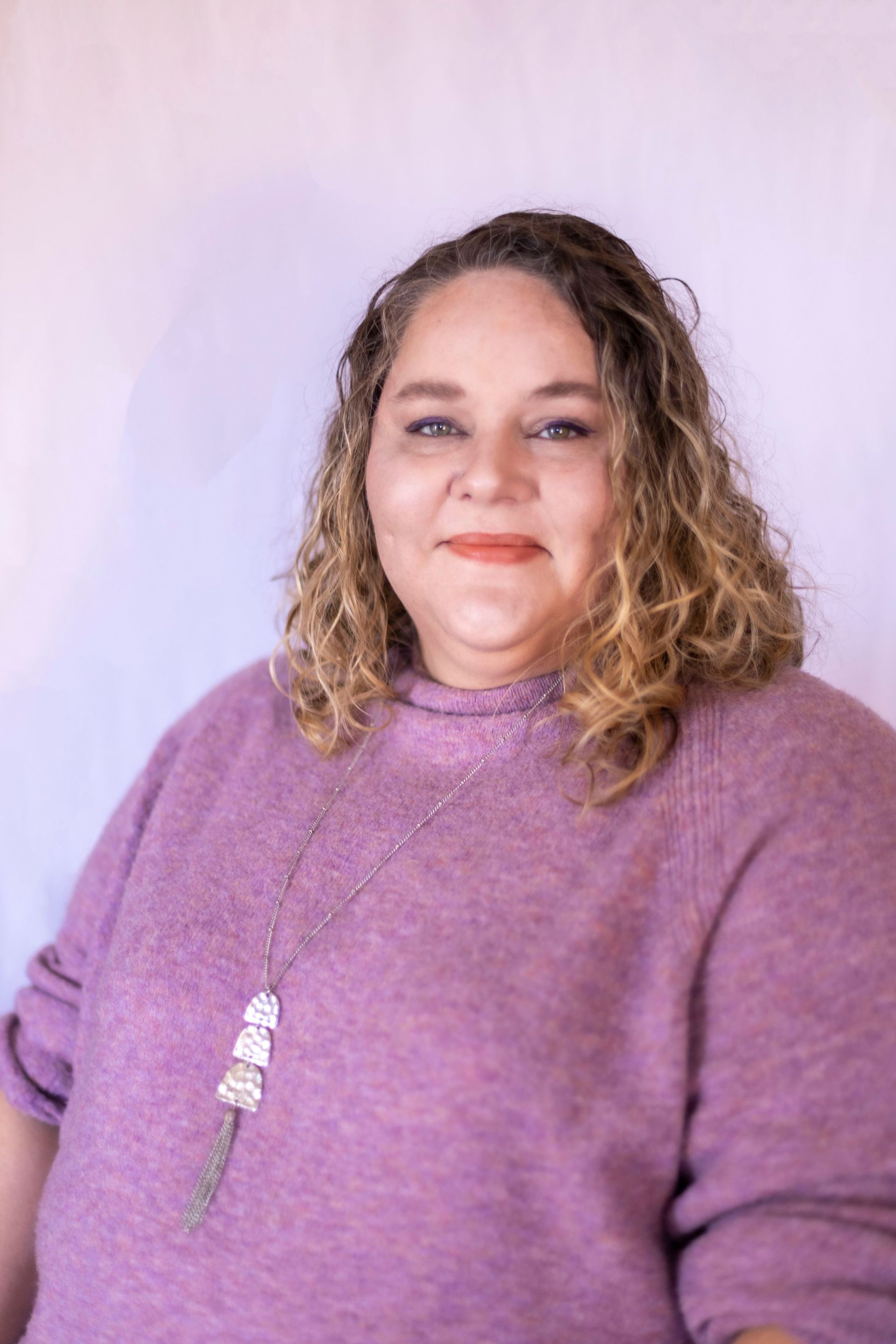 A woman is wearing a purple sweater and a necklace.