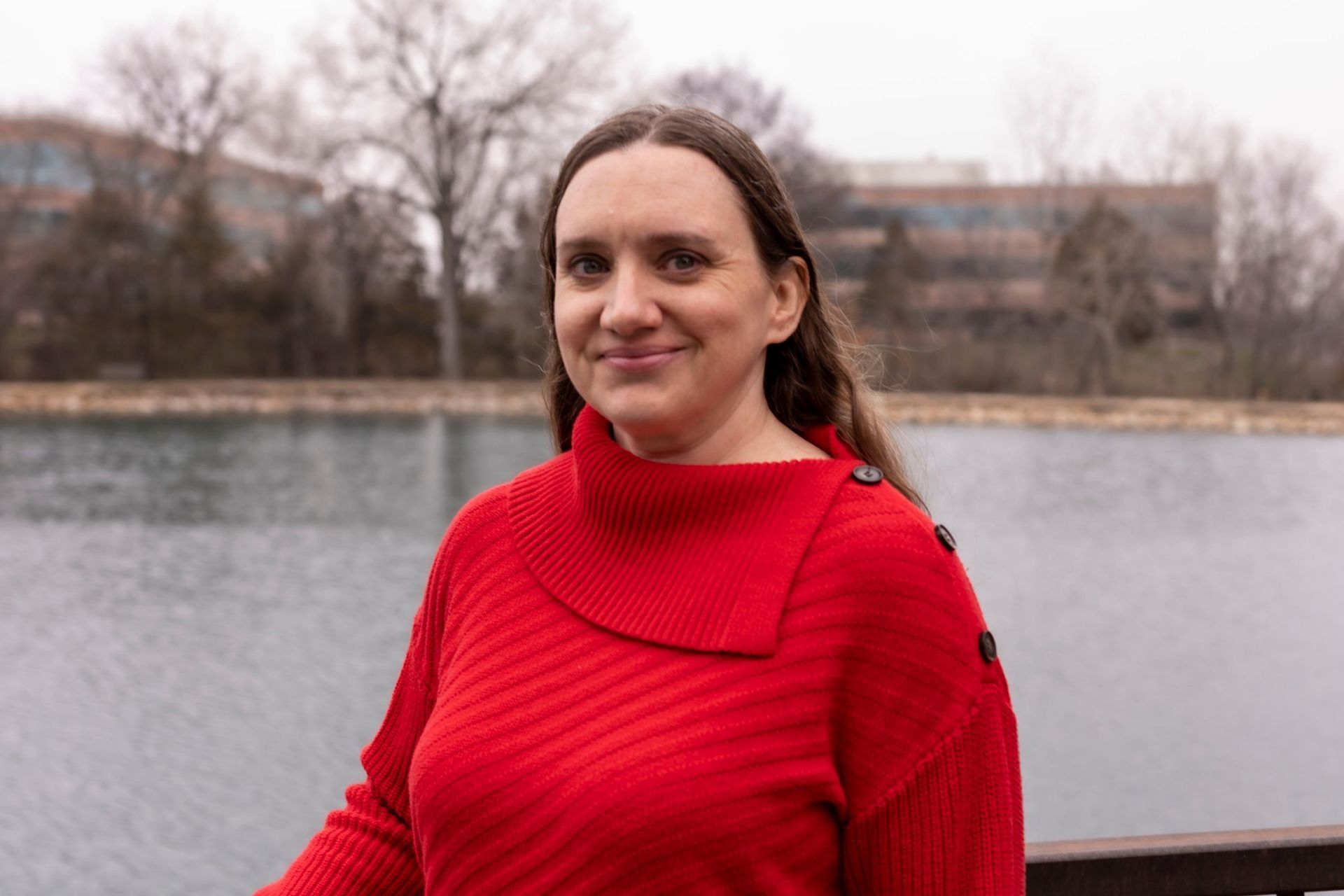 A woman in a red sweater is standing next to a body of water.