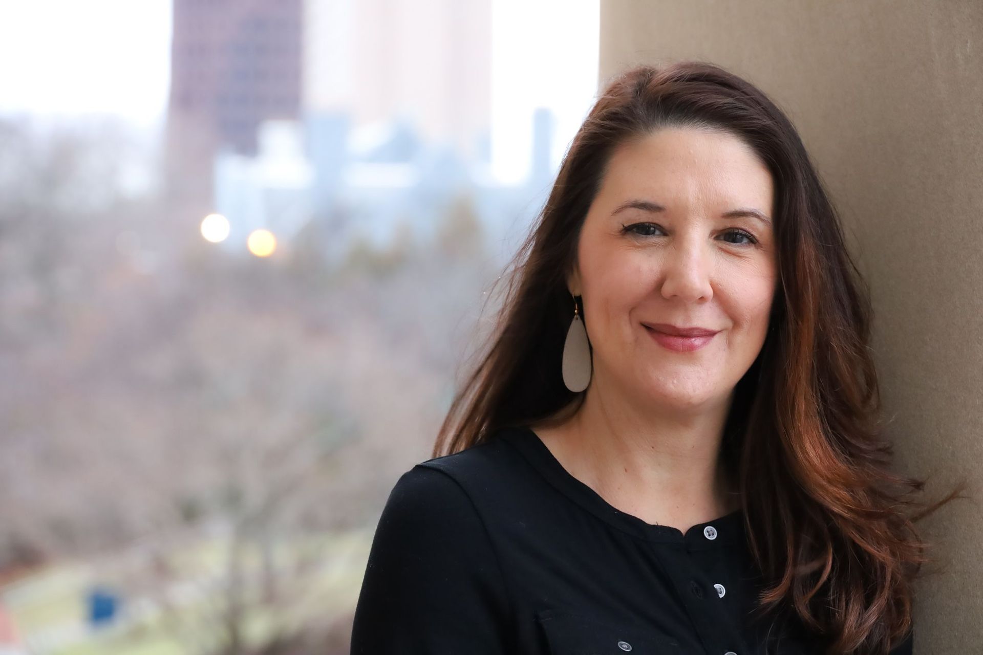 A woman in a black shirt is leaning against a wall and smiling.