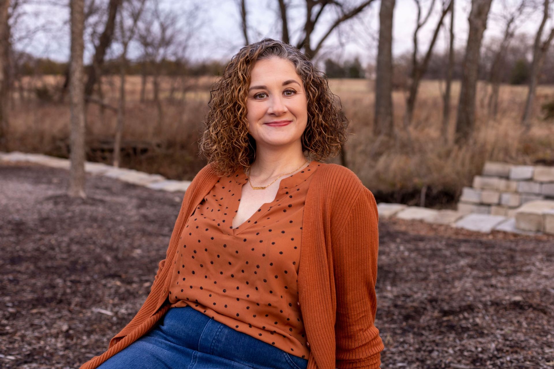 A woman is sitting on the ground wearing a polka dot shirt and a cardigan.
