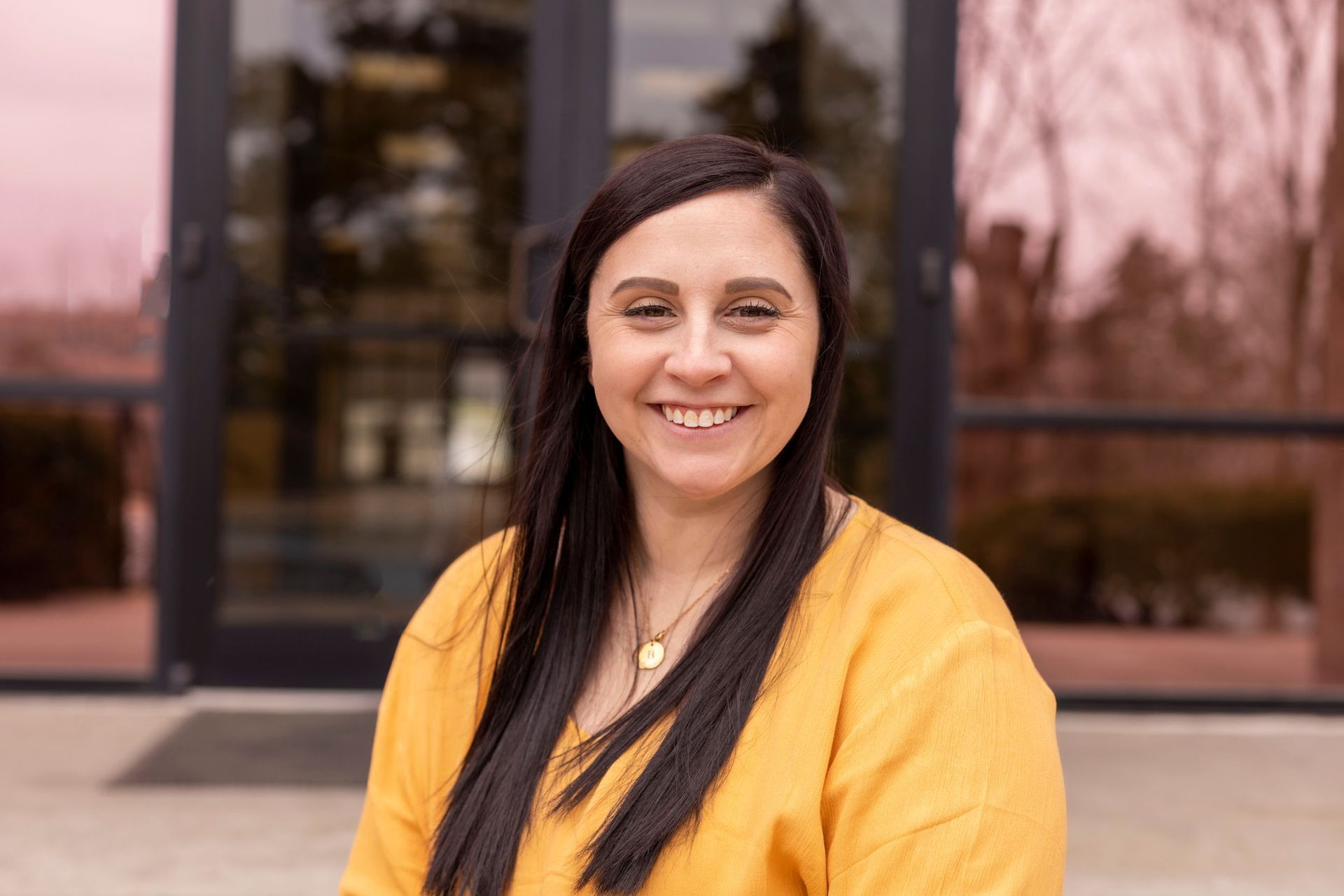 A woman in a yellow shirt is smiling in front of a building.