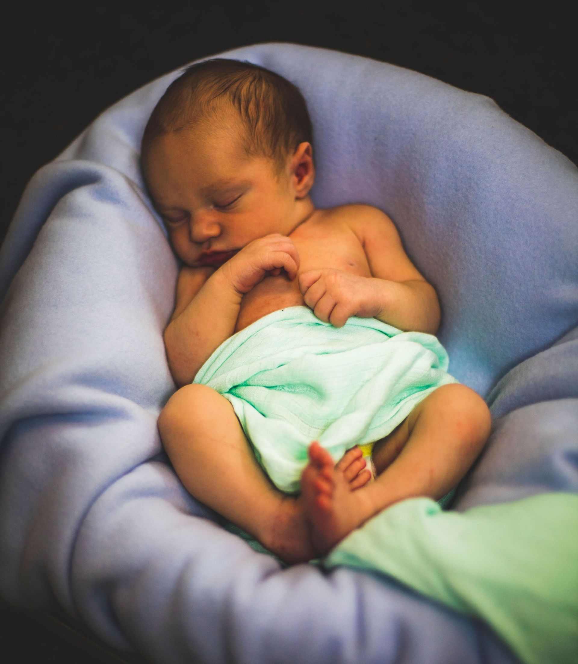 A baby wrapped in a green blanket is sleeping in a basket