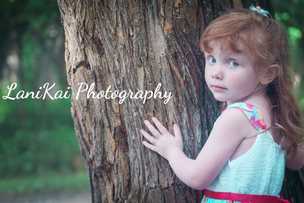 A little girl is standing next to a tree trunk.