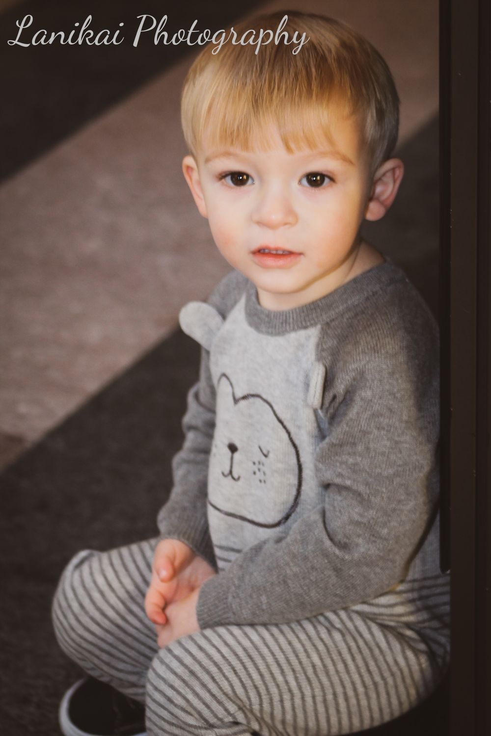 A young boy wearing a bear sweater sits on the floor