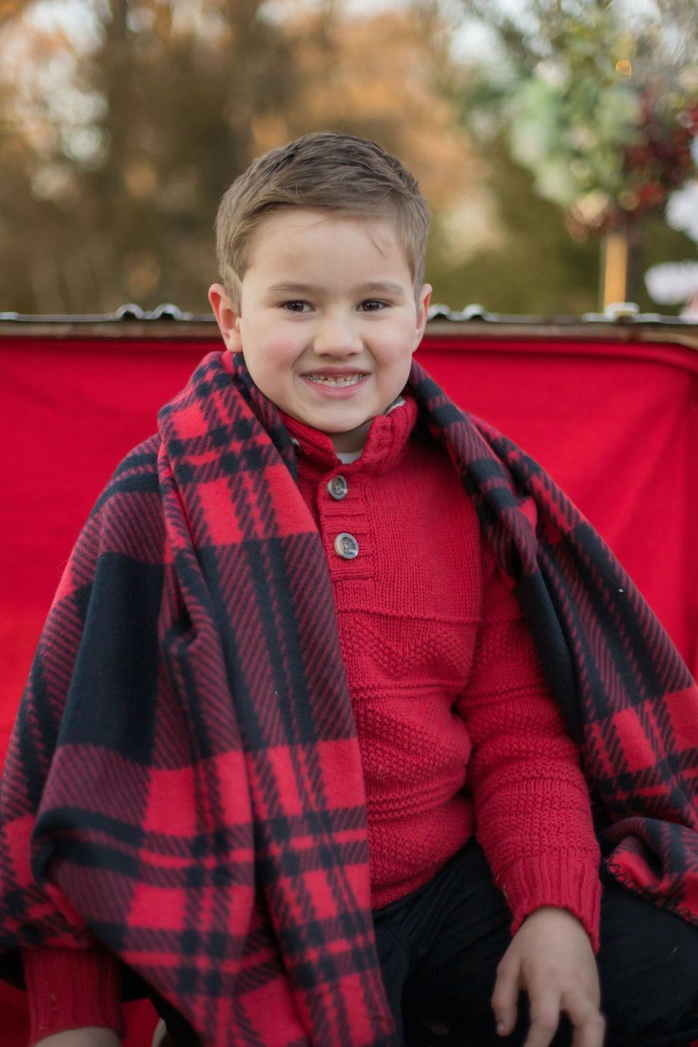 A young boy is wrapped in a red and black plaid blanket.