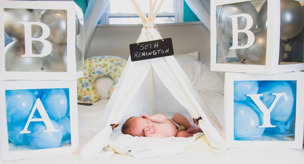 A baby is sleeping in a teepee surrounded by balloons.