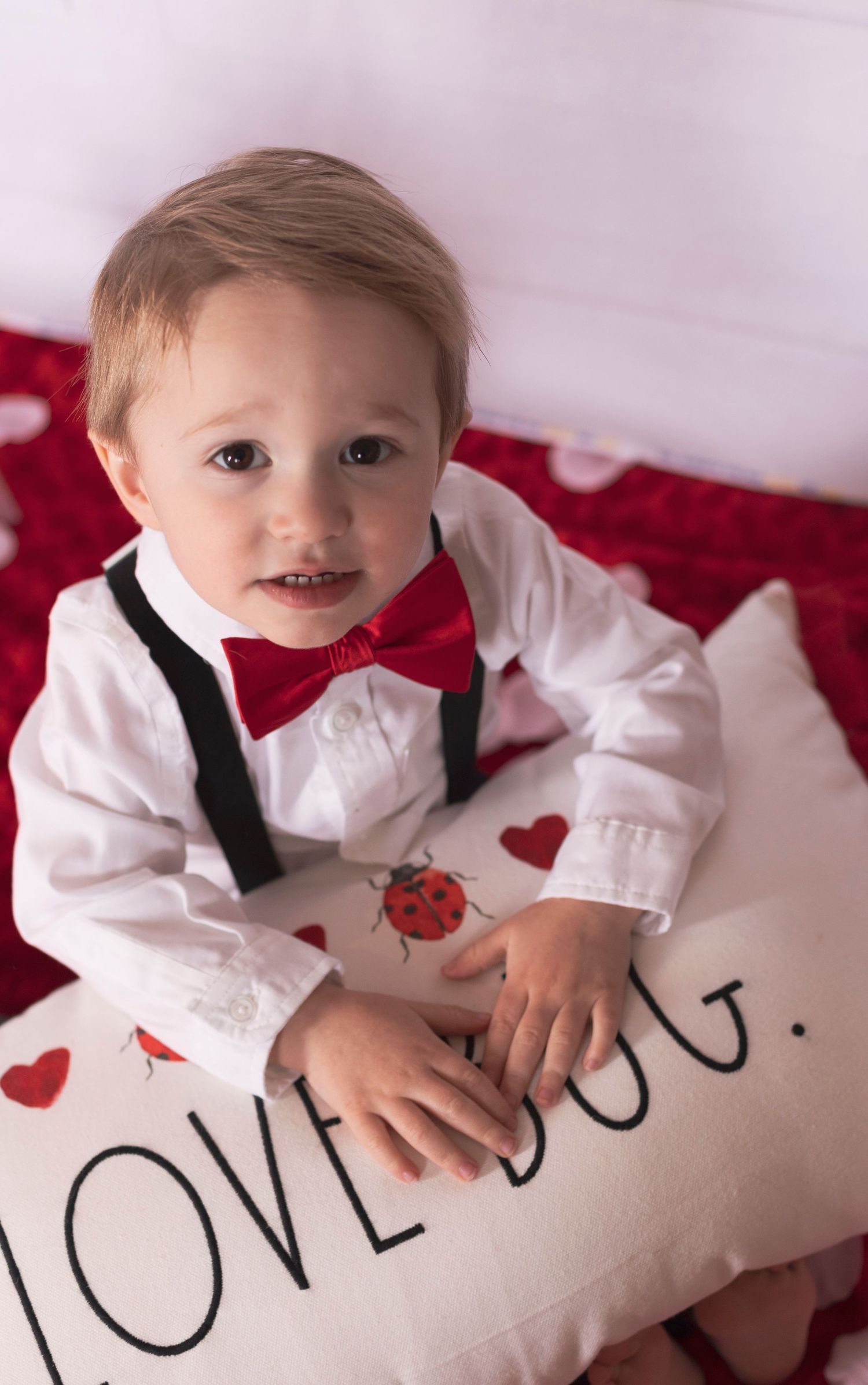 A little boy is sitting on a pillow that says love bug