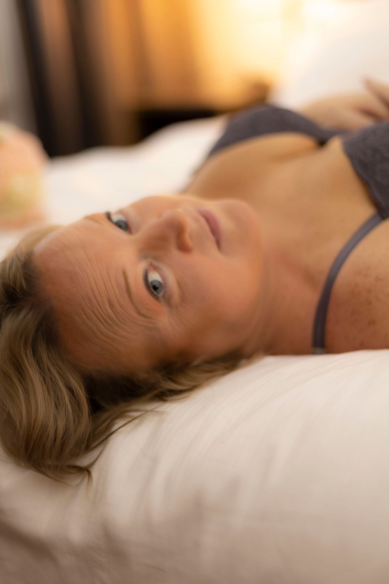 A woman in a bra is laying on a bed with her head on a pillow.