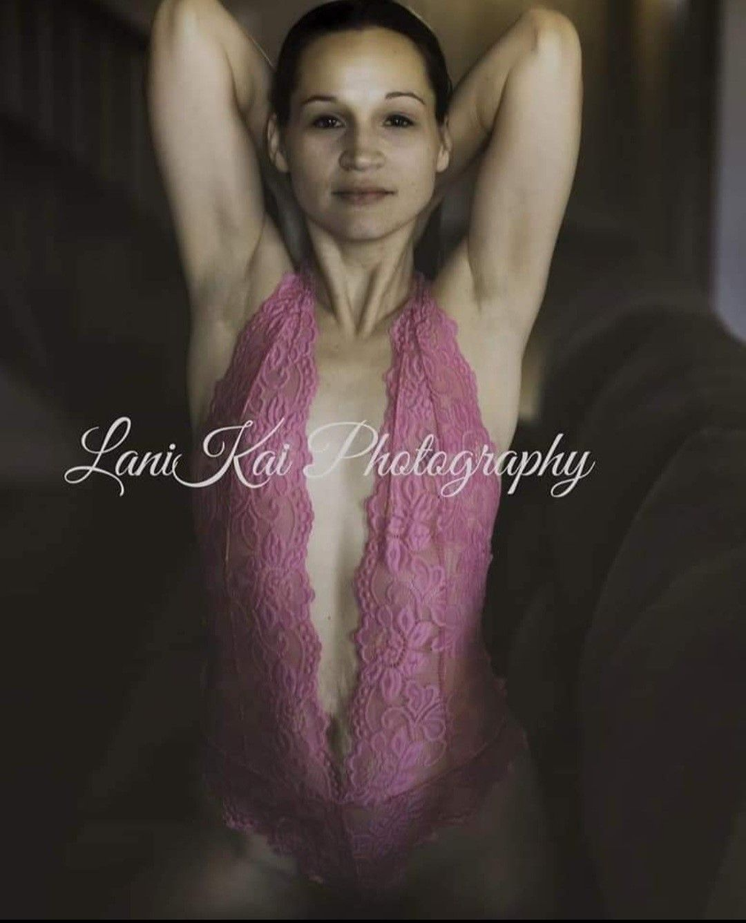 A woman in a pink lace bodysuit is sitting on a couch.