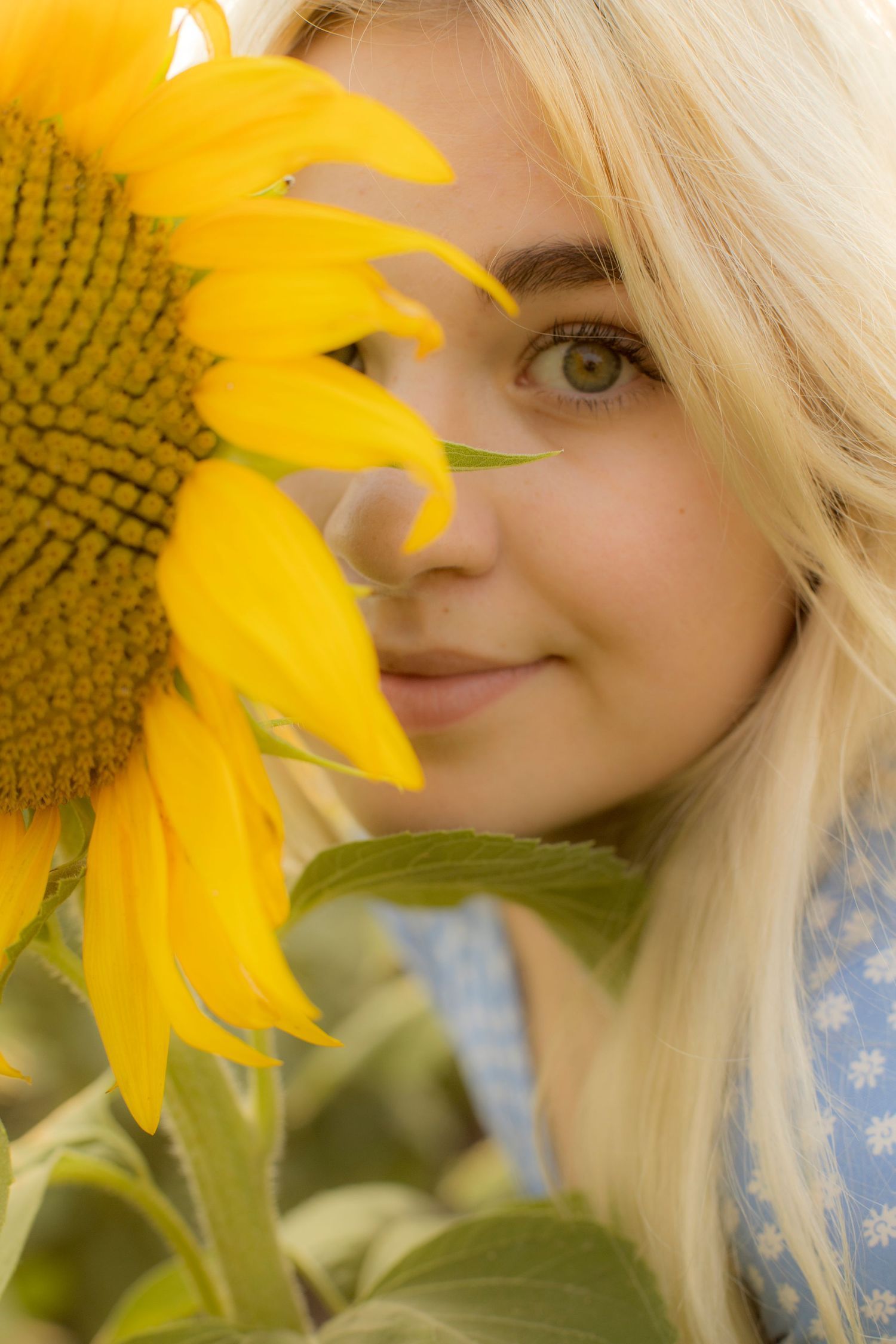 A woman is holding a sunflower in front of her face.