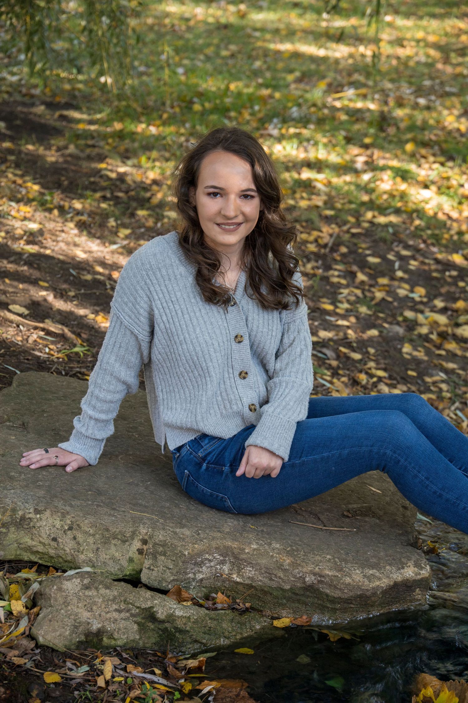 A young woman is sitting on a rock in a park.