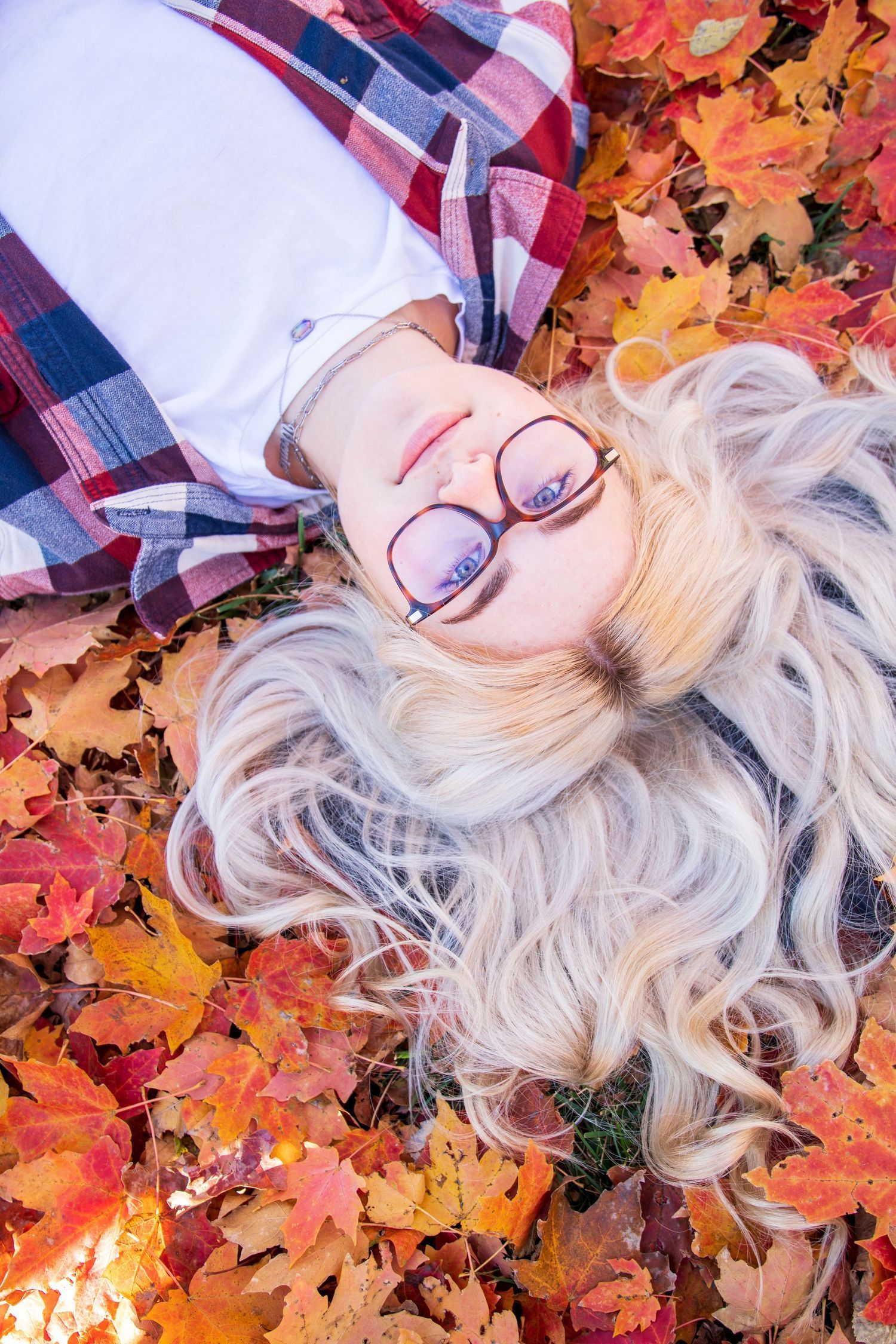 A woman is laying on her back in a pile of leaves.