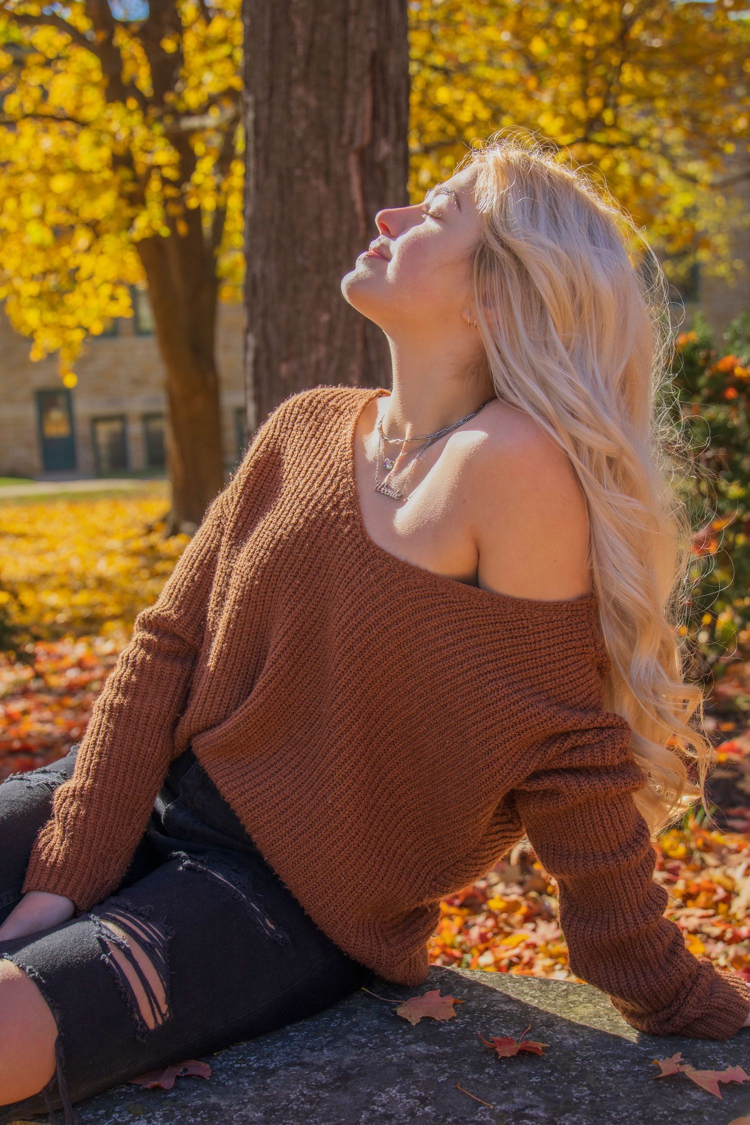 A woman in a brown sweater is sitting on the ground in front of a tree.
