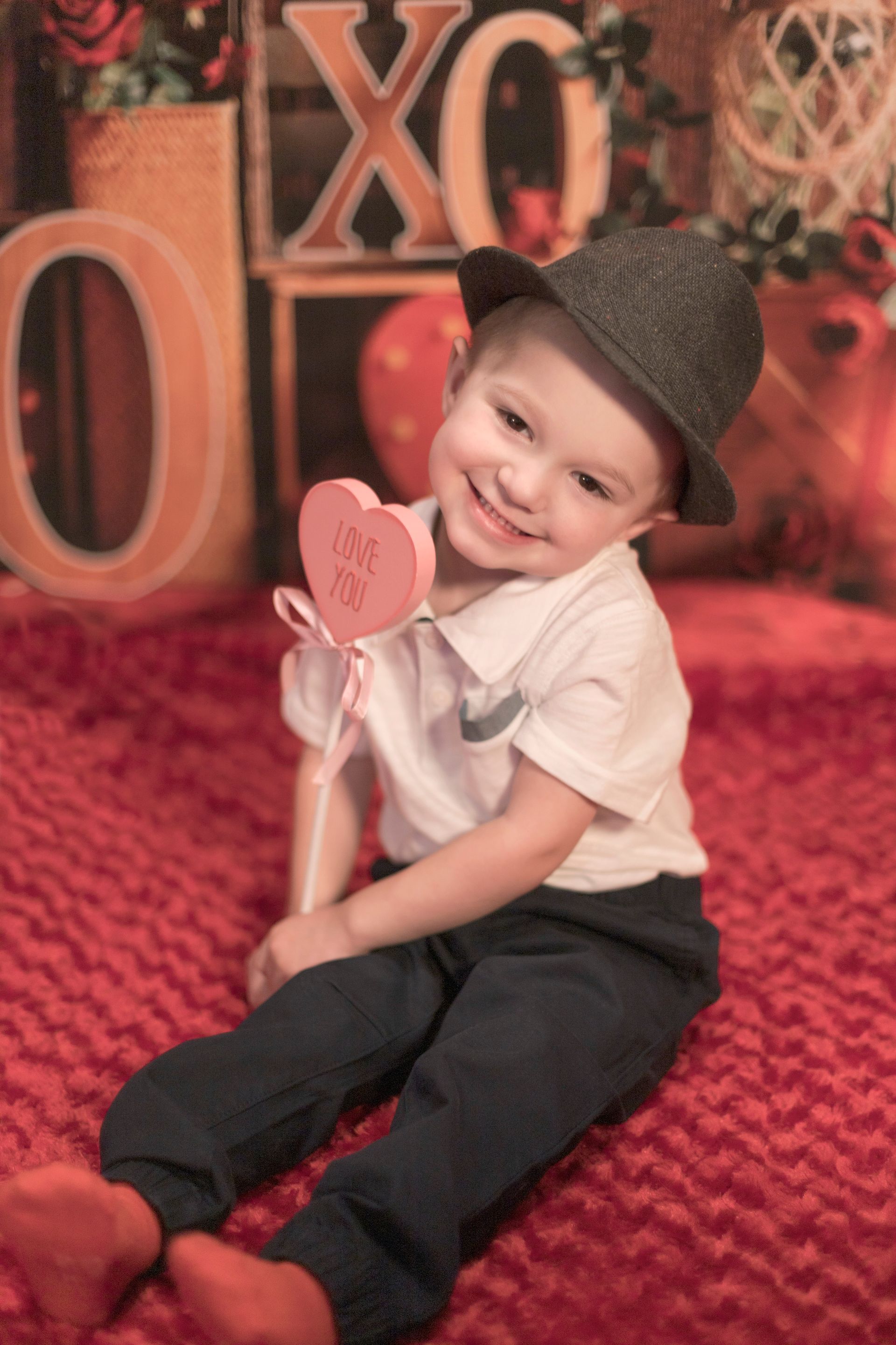 A little boy wearing a hat is holding a heart shaped lollipop that says i love you