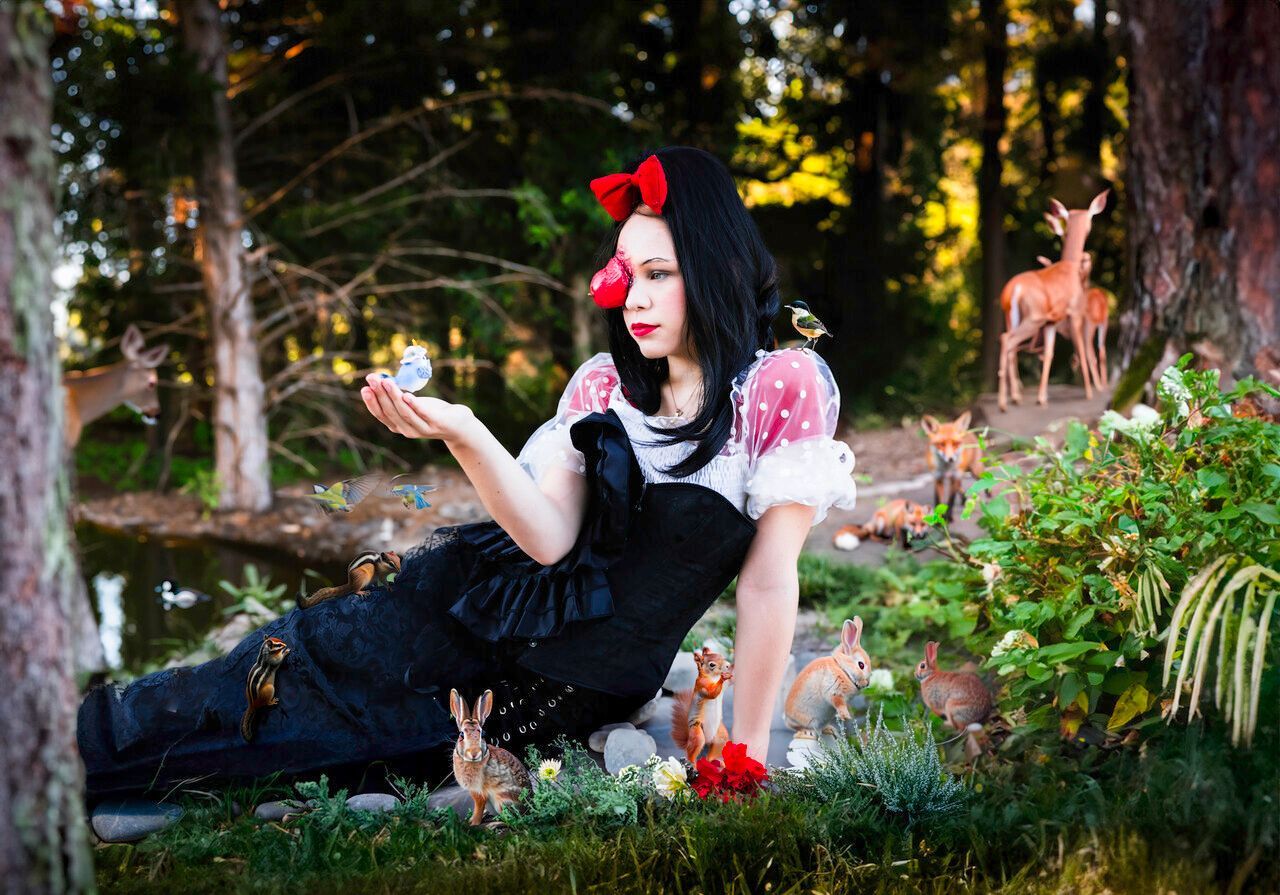 A woman in a snow white costume is laying in the grass holding a butterfly.