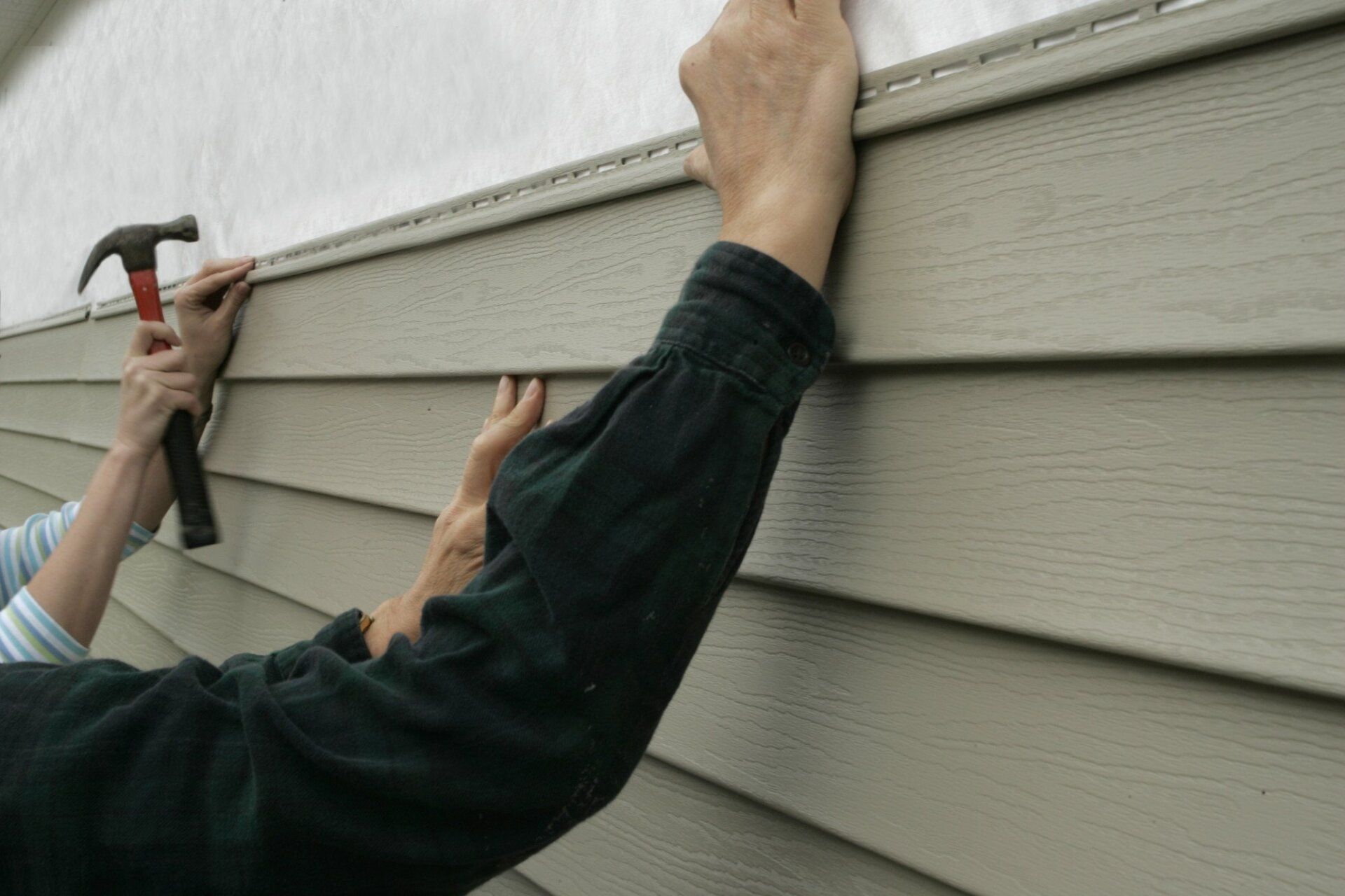 A group of workers installing siding on a house.