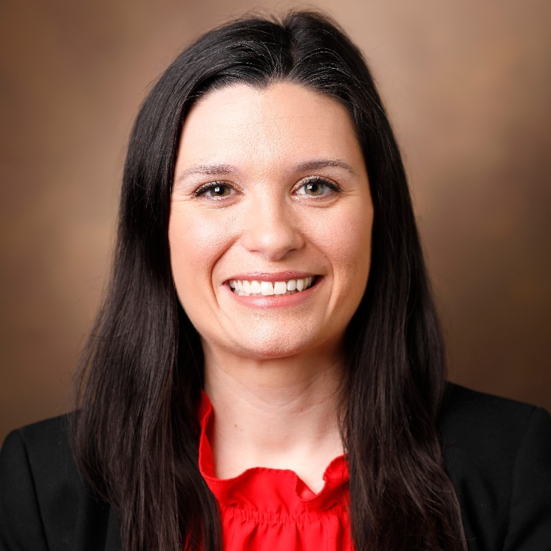 Dan Sharp wearing a blue shirt and black blazer posing for a headshot against a gray background.