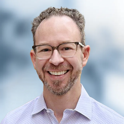 A man with a beard is wearing a white shirt and smiling for the camera.