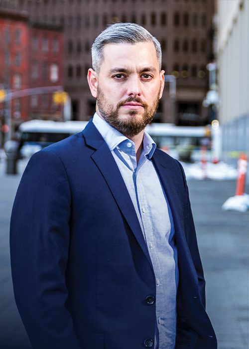 A man in a suit and sweater is standing on a city street.