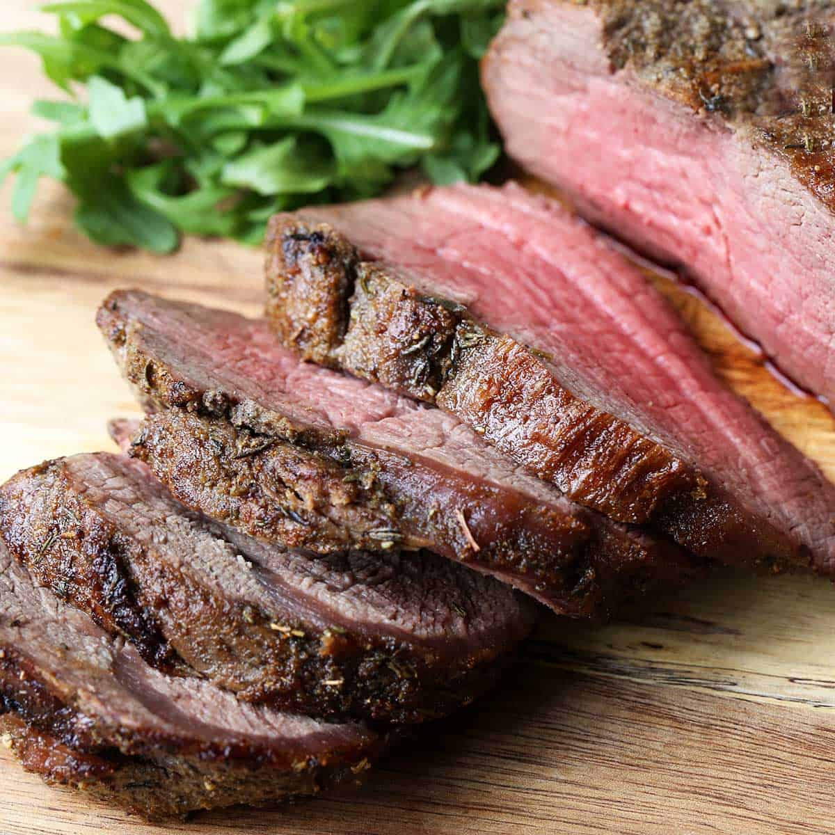 A close up of sliced steak on a wooden cutting board.