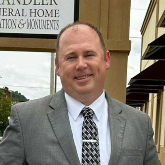A man in a suit and tie stands in front of a funeral home sign