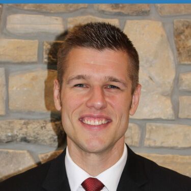 A man in a suit and tie is smiling in front of a stone wall