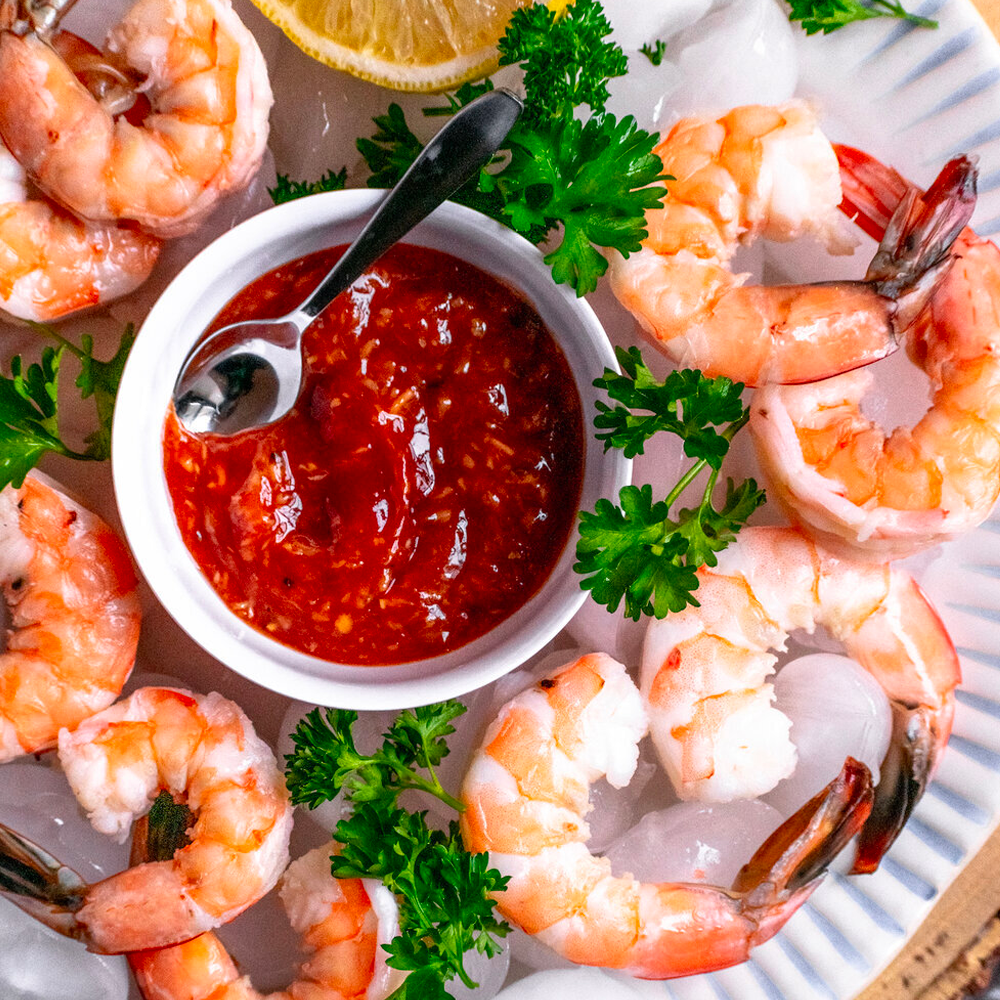 A plate of shrimp with a bowl of sauce and a spoon