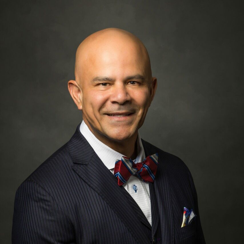 A bald man in a suit and bow tie is smiling for the camera.