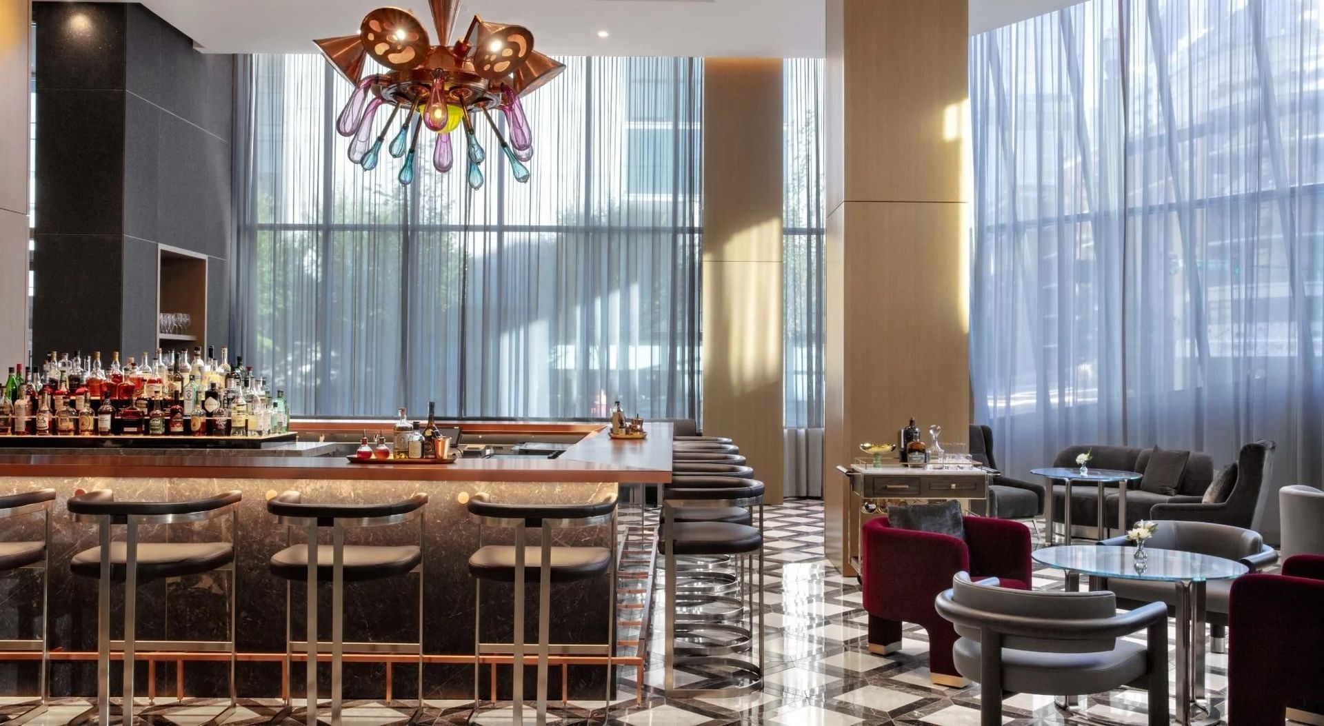 A restaurant with a bar , chairs , tables and a chandelier.