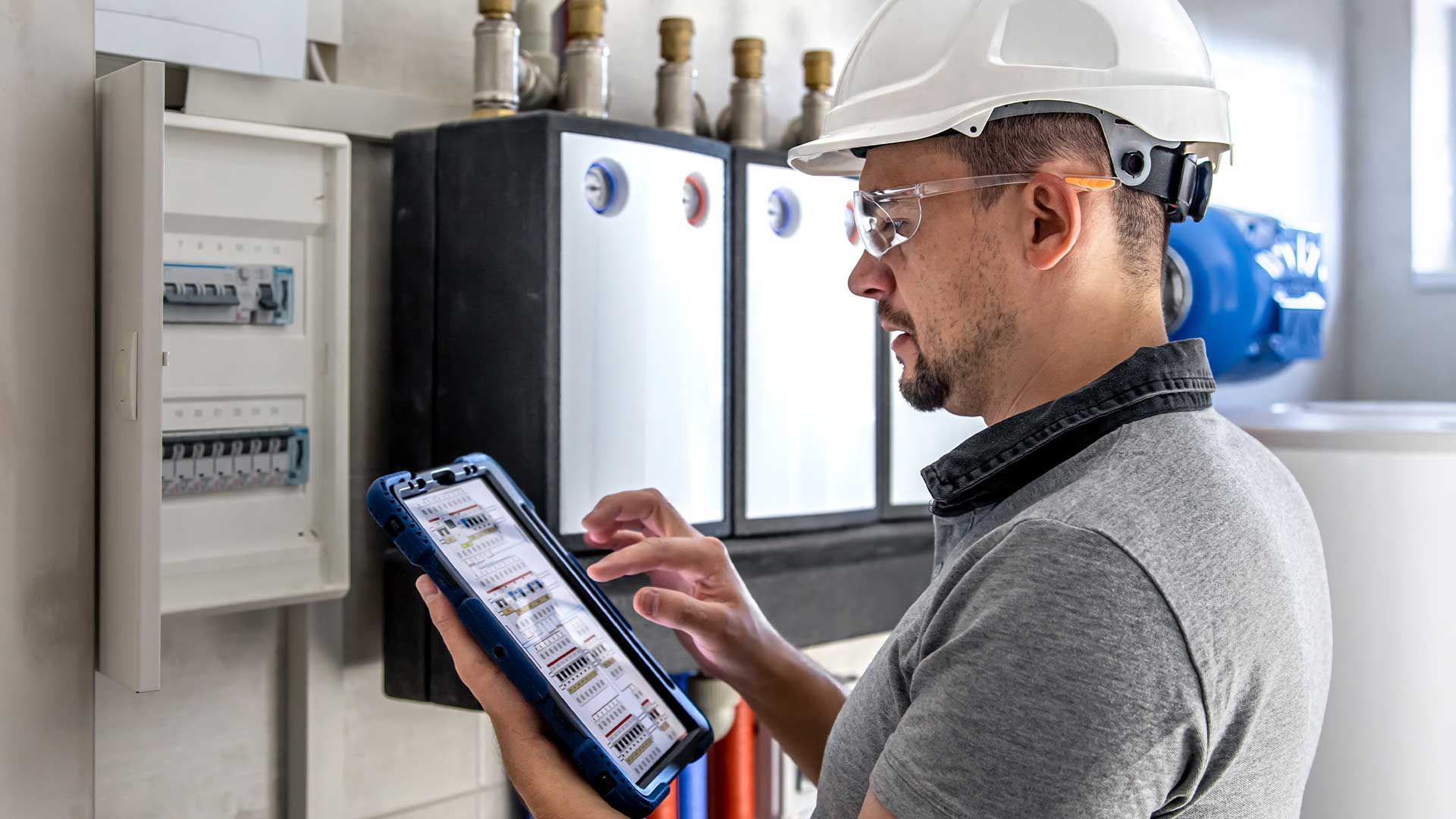 A man wearing a hard hat and safety glasses is using a tablet computer.