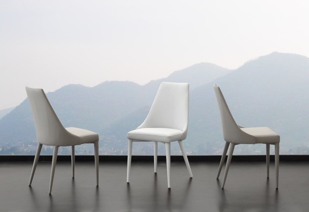 Tre sedie bianche sono posizionate davanti a una finestra con le montagne sullo sfondo.