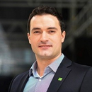 A man in a blazer and button-up shirt smiles at the camera. 