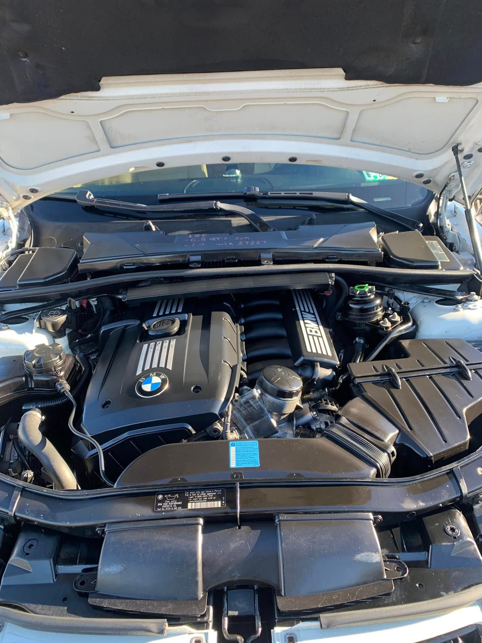 Open hood of a BMW engine. The engine bay is clean, and the car is white.