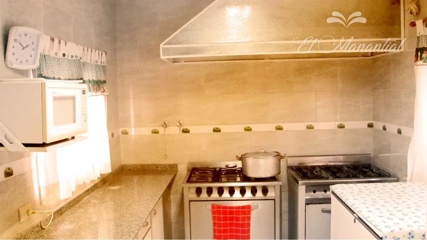 Una cocina con encimera, microondas, fogones con una toalla roja y campana extractora 