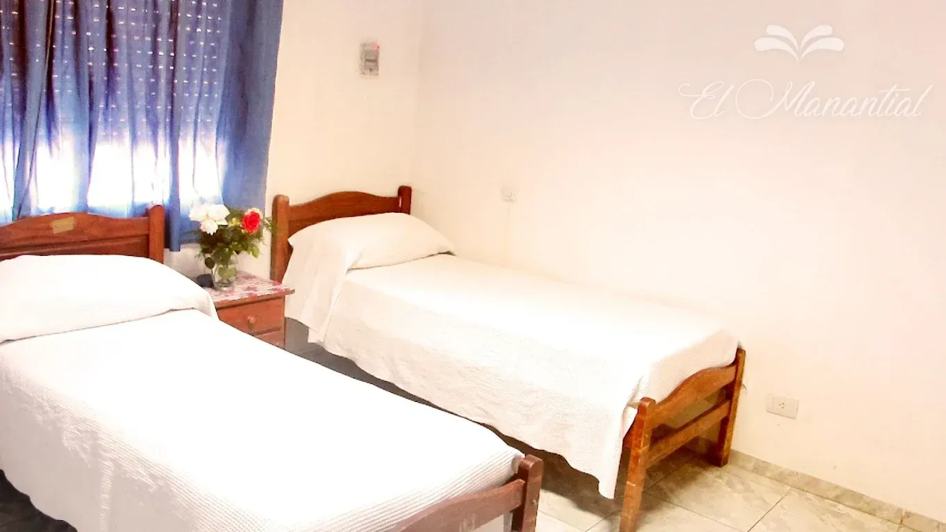 Dos camas individuales con ropa de cama blanca, dispuestas una al lado de la otra en una habitación sencilla 